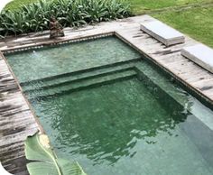 an empty swimming pool in the middle of a yard with lounge chairs and plants around it