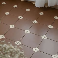 a vase filled with white flowers sitting on top of a brown tiled floor next to a window