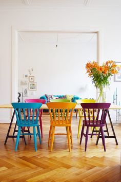 colorful chairs are arranged around a table in the middle of a room with hardwood floors