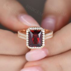 a woman's hand holding an engagement ring with a red stone in the center