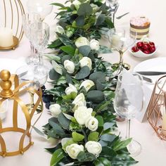 the table is set with white roses and greenery for a festive dinner party