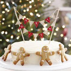 a decorated cake with gingerbreads and bunting flags on it, sitting in front of a christmas tree