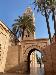 a tall tower with a clock on it's side next to palm trees and a brick wall