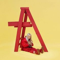 a woman sitting on the ground in front of a red wooden structure with her legs crossed