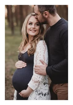 a pregnant couple cuddles in the woods