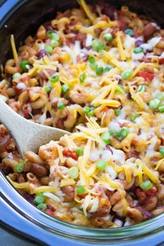 a crock pot filled with macaroni and cheese on top of green onions