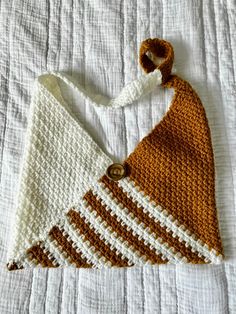 a crocheted triangle is laying on top of a white bed sheet with a button in the middle