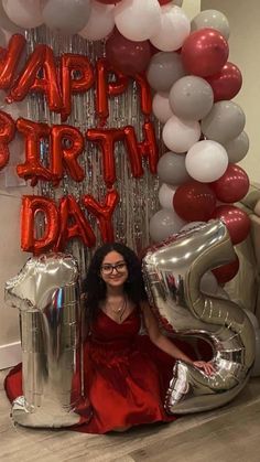 a woman sitting on the floor with balloons in front of her and an air filled balloon arch behind her