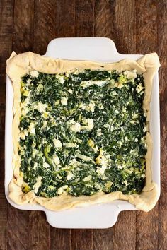 spinach and artichoke quiche in a white casserole dish on a wooden table