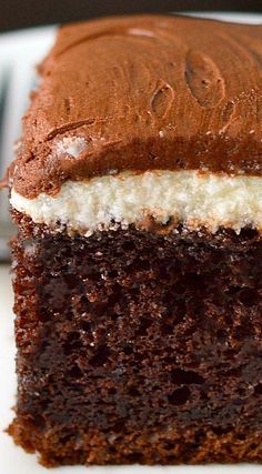 a piece of chocolate cake with white frosting on a plate next to a fork