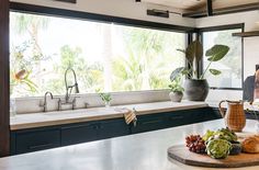 a kitchen counter with various fruits and vegetables on it, in front of a large window