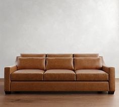 a brown leather couch sitting on top of a hard wood floor next to a white wall