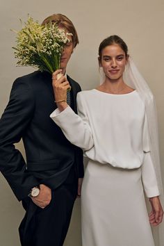 a man and woman standing next to each other in front of a wall holding flowers