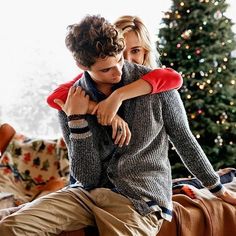 a young man and woman embracing each other in front of a christmas tree with lights