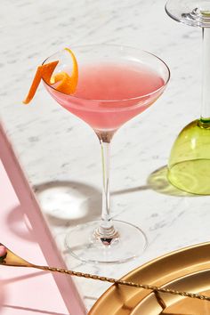 two martinis with an orange garnish sit next to each other on a marble table