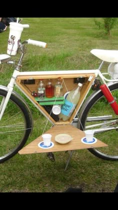 a bicycle with a beer cooler attached to the back and people sitting on the grass behind it