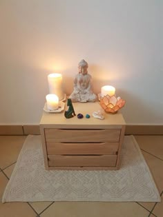 a table with two candles and a buddha statue on it in front of a white wall