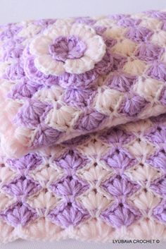 a purple and white crocheted blanket with a flower on the top, folded up