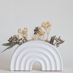 a white vase with flowers in it and a rainbow shaped planter on the side