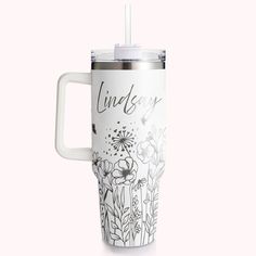 a white travel mug with flowers and the words june on it's side, in front of a pink background