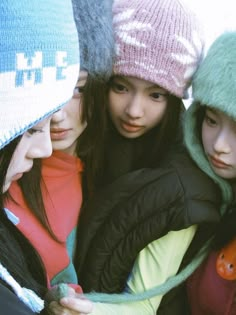 three young women are huddled together wearing winter hats