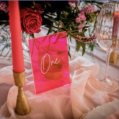 a pink card sitting on top of a table next to a wine glass and candle