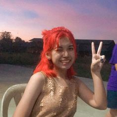 a woman with red hair sitting in a chair making the peace sign