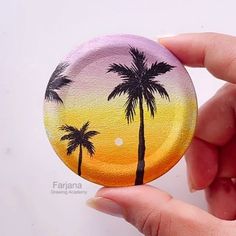 a hand holding a button with palm trees painted on it