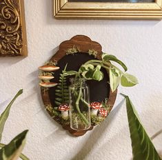 a wooden clock with plants and mushrooms on the wall next to a planter in a vase