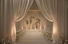 a wedding ceremony with white flowers and candles in front of the aisle lined with drapes