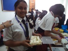 two girls in uniforms are serving themselves food at a school luncheon table with other students