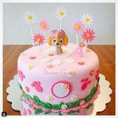 a pink birthday cake decorated with flowers and a dog figurine on the top