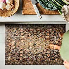 a woman standing on top of a rug in front of a table with vegetables and utensils