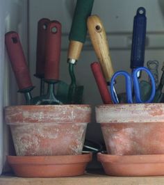 two clay pots with scissors and other items in them sitting on a shelf next to each other