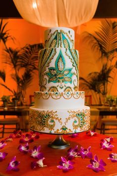 a white and gold wedding cake with purple flowers on the table in front of it