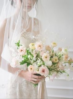 a woman in a wedding dress holding a bouquet of white and pink flowers with veil over her head