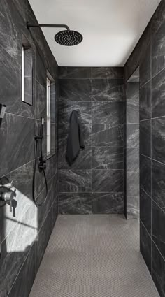 a walk in shower sitting next to a black tiled wall with a hand held shower head