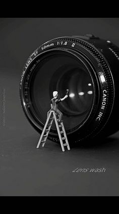 a miniature man standing on top of a camera with a ladder in front of it