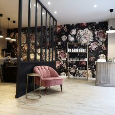 a pink chair sitting in front of a wall with flowers on it