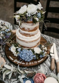 a wedding cake sitting on top of a wooden table next to flowers and knifes