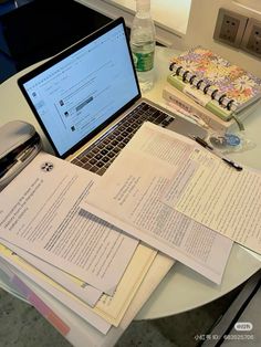 an open laptop computer sitting on top of a table next to books and papers that have been placed on it