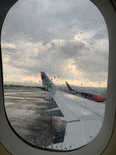 an airplane window looking out at the wing and water droplets on the glass as seen from inside