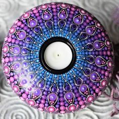 a candle is sitting on top of a decorative object with purple, blue and pink designs