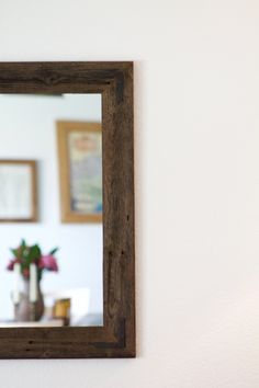 a mirror hanging on the wall above a table with flowers in vases and other items