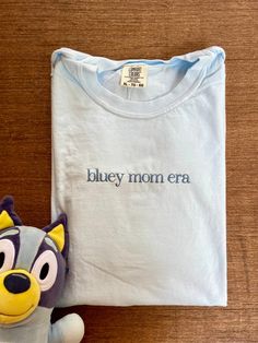 Bluey mom era with long dog on the sleeve!  This high quality comfort colors shirt is made to get softer with each wash and each shirt is embroidered by me. Shirts are made with love and care and made to order. Snag yours now for a unique fashion statement. Light Wash Cotton T-shirt, Casual T-shirt With Custom Embroidery For Everyday, Casual Everyday T-shirt With Custom Embroidery, Family Matching Cotton Tops With Custom Embroidery, Light Blue Embroidered Cotton Tops, Blue Cotton Tops With Custom Embroidery, Blue Cotton Family Matching T-shirt, Vintage Embroidered Cotton T-shirt, Everyday Cotton Tops With Embroidered Text