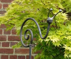 an iron sculpture in front of a brick wall with green leaves on the tree branches