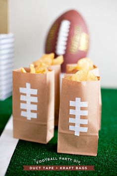 two brown paper bags filled with food sitting on top of a green field next to a football