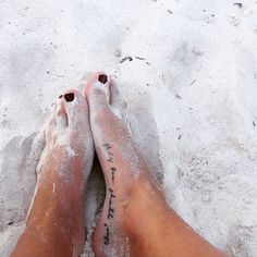 a person's feet covered in white sand with writing on the bottom and foot