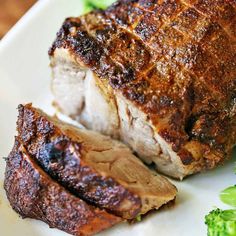 a piece of meat on a plate with broccoli next to it and another piece of meat in the background