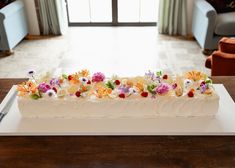 a white cake with flowers on it sitting on a table in front of a couch